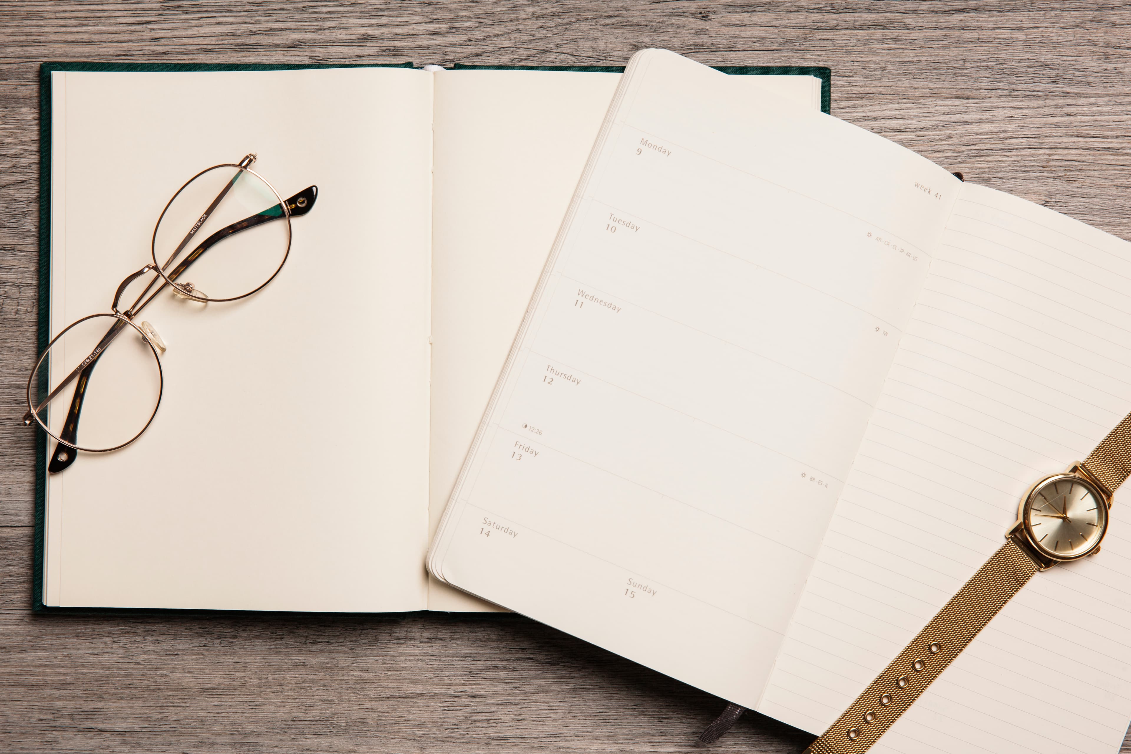 An open notebook, reading glasses and a planner on a desk